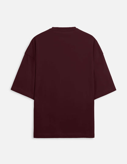 Deep maroon or burgundy oversized unisex t-shirt featuring a small, centered graphic of the Hindi text "भंडलोक" (Bhandlok - Wild/Drunk People) in light red, topped with a small red dot. Soft cotton, drop-shoulder, boxy casual apparel with a party-themed or humorous typographic design.