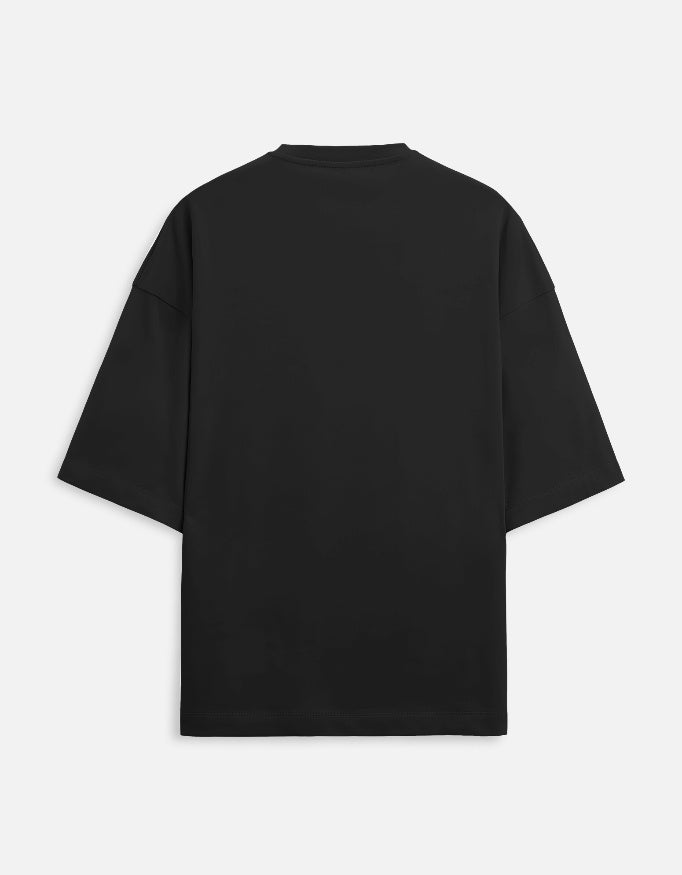 Color_Black. Oversized black streetwear t-shirt featuring a small rectangular graphic on the chest of a surrealist monochromatic figure with a pink tongue. Features dropped shoulders, heavyweight cotton fabric, and a boxy fit.