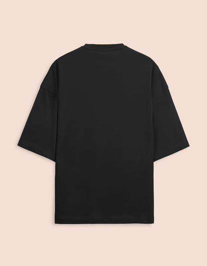 Black oversized unisex t-shirt featuring a centered, small graphic of the text "Nirogi Aatma" (Healthy Soul) written in bold red lettering. Soft cotton, drop-shoulder, boxy casual apparel with a spiritual or motivational typographic design.
