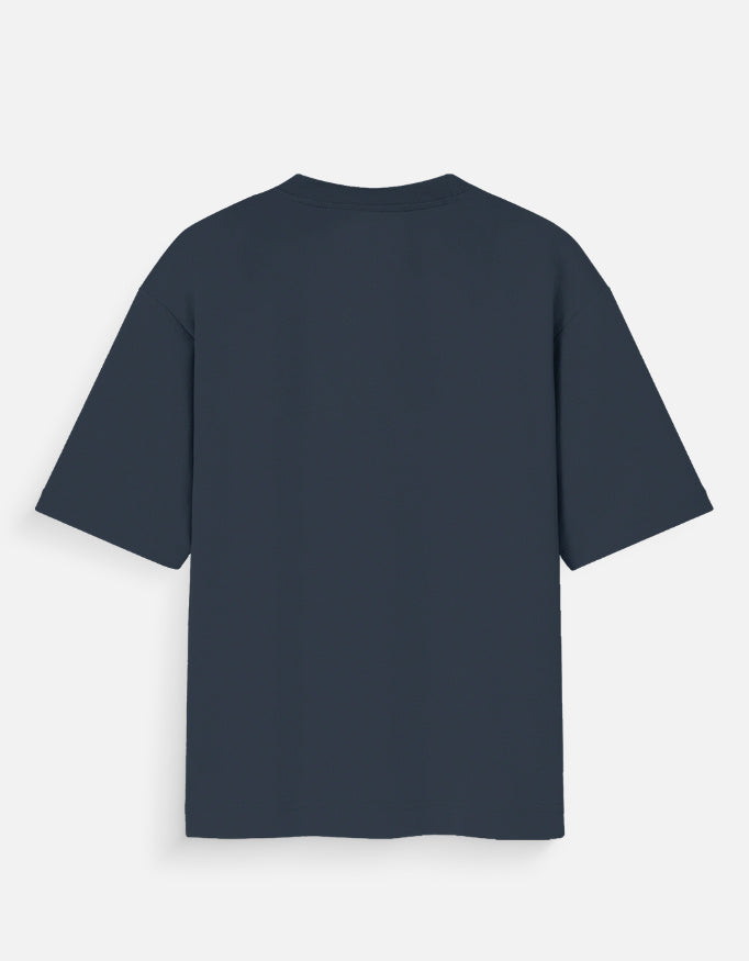 Navy Blue oversized unisex t-shirt featuring a centered, small graphic of the word "Aalasya" (laziness) written in red, stylized text with a red strikethrough line, signifying "No Laziness." Soft cotton, drop-shoulder, boxy casual apparel with ironic or statement typography.