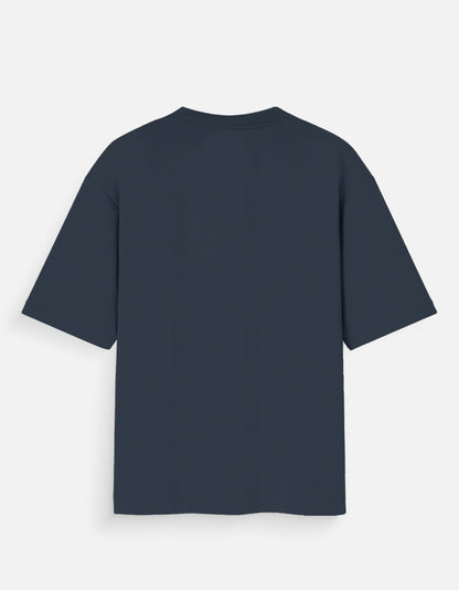 Navy Blue oversized unisex t-shirt featuring a centered, small graphic of the word "Aalasya" (laziness) written in red, stylized text with a red strikethrough line, signifying "No Laziness." Soft cotton, drop-shoulder, boxy casual apparel with ironic or statement typography.