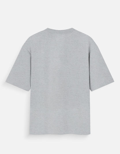 Heather grey oversized unisex t-shirt featuring a centered, small graphic of the word "Aalasya" (laziness) written in red, stylized text with a red strikethrough line, signifying "No Laziness." Soft cotton, drop-shoulder, boxy casual apparel with ironic or statement typography.