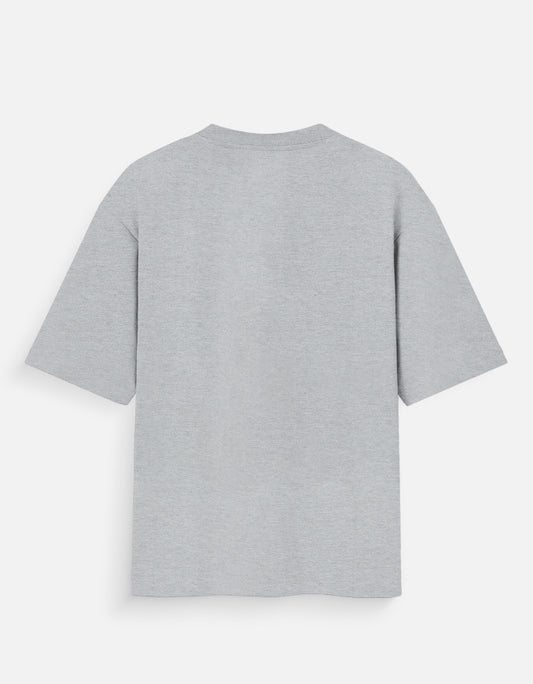 Heather grey oversized unisex t-shirt featuring a centered, small graphic of the word "Aalasya" (laziness) written in red, stylized text with a red strikethrough line, signifying "No Laziness." Soft cotton, drop-shoulder, boxy casual apparel with ironic or statement typography.