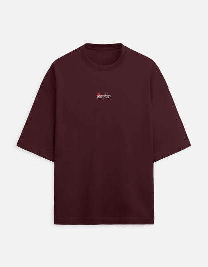 Deep maroon or burgundy oversized unisex t-shirt featuring a small, centered graphic of the Hindi text "भंडलोक" (Bhandlok - Wild/Drunk People) in light red, topped with a small red dot. Soft cotton, drop-shoulder, boxy casual apparel with a party-themed or humorous typographic design.