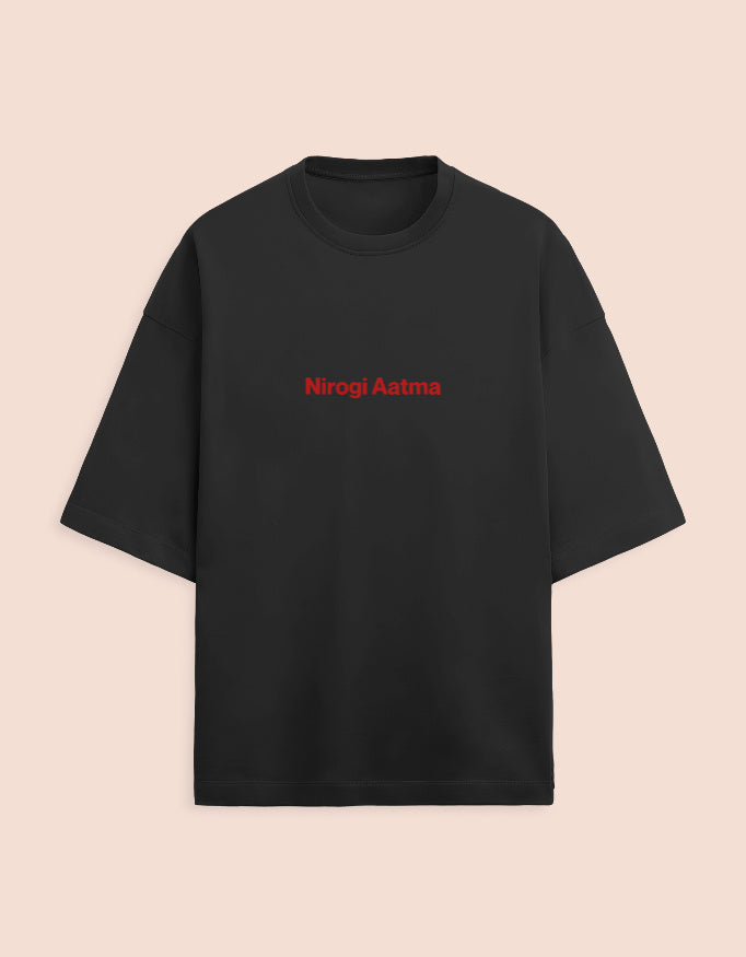 Black oversized unisex t-shirt featuring a centered, small graphic of the text "Nirogi Aatma" (Healthy Soul) written in bold red lettering. Soft cotton, drop-shoulder, boxy casual apparel with a spiritual or motivational typographic design.