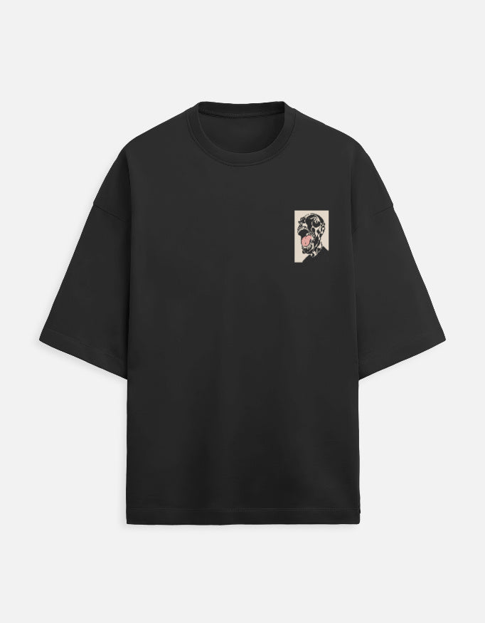 Color_Black. Oversized black streetwear t-shirt featuring a small rectangular graphic on the chest of a surrealist monochromatic figure with a pink tongue. Features dropped shoulders, heavyweight cotton fabric, and a boxy fit.