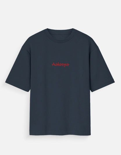 Navy Blue oversized unisex t-shirt featuring a centered, small graphic of the word "Aalasya" (laziness) written in red, stylized text with a red strikethrough line, signifying "No Laziness." Soft cotton, drop-shoulder, boxy casual apparel with ironic or statement typography.