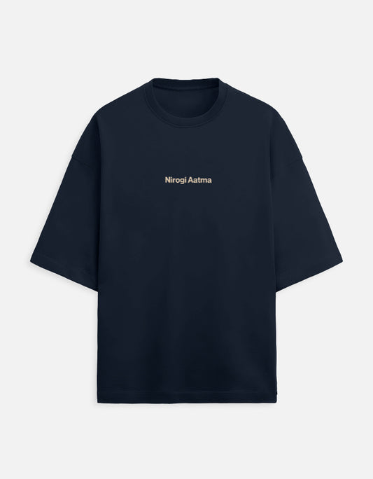 Navy Blue oversized unisex t-shirt featuring a centered, small graphic of the text "Nirogi Aatma" (Healthy Soul) written in light brown or gold lettering. Soft cotton, drop-shoulder, boxy casual apparel with a spiritual or motivational typographic design.