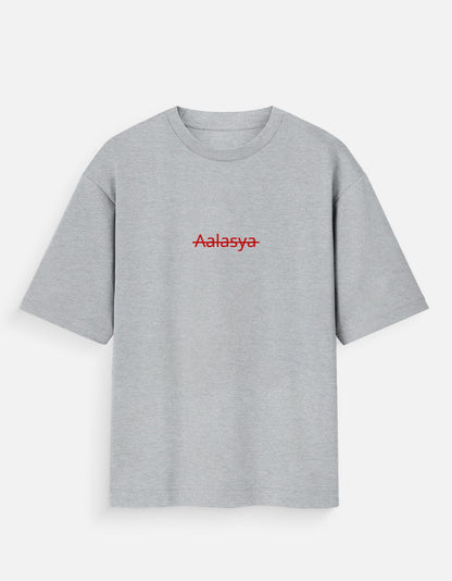 Heather grey oversized unisex t-shirt featuring a centered, small graphic of the word "Aalasya" (laziness) written in red, stylized text with a red strikethrough line, signifying "No Laziness." Soft cotton, drop-shoulder, boxy casual apparel with ironic or statement typography.