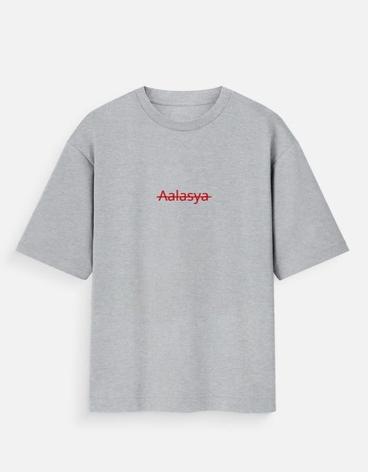 Heather grey oversized unisex t-shirt featuring a centered, small graphic of the word "Aalasya" (laziness) written in red, stylized text with a red strikethrough line, signifying "No Laziness." Soft cotton, drop-shoulder, boxy casual apparel with ironic or statement typography.