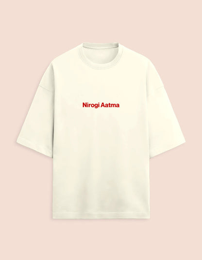 Cream or off-white oversized unisex t-shirt featuring a centered, small graphic of the text "Nirogi Aatma" (Healthy Soul) written in bold red lettering. Soft cotton, drop-shoulder, boxy casual apparel with a spiritual or motivational typographic design.
