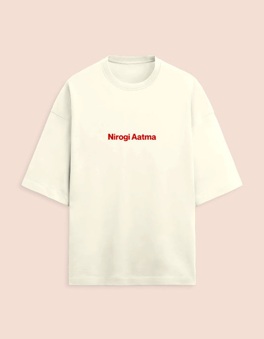 Cream or off-white oversized unisex t-shirt featuring a centered, small graphic of the text "Nirogi Aatma" (Healthy Soul) written in bold red lettering. Soft cotton, drop-shoulder, boxy casual apparel with a spiritual or motivational typographic design.