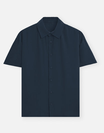 Color_NavyBlue. Premium unisex oversized button-down shirt with a wide, boxy fit and dropped shoulders. Made from breathable solid-colored cotton. Features a structured collar and longline hem, perfect for layered streetwear or minimalist smart-casual outfits.