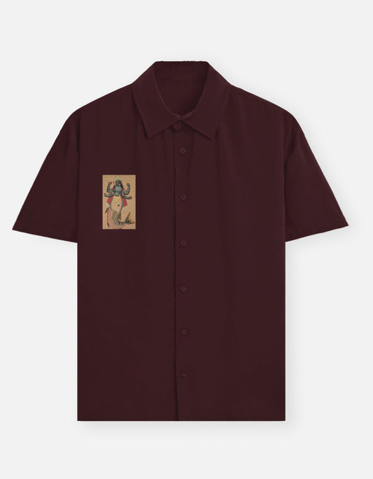 Color_Maroon. Deep burgundy short-sleeve button-down shirt featuring a centered chest graphic of the Matsya avatar. Premium lightweight fabric with a camp collar and relaxed silhouette. Iconic heritage-inspired streetwear.